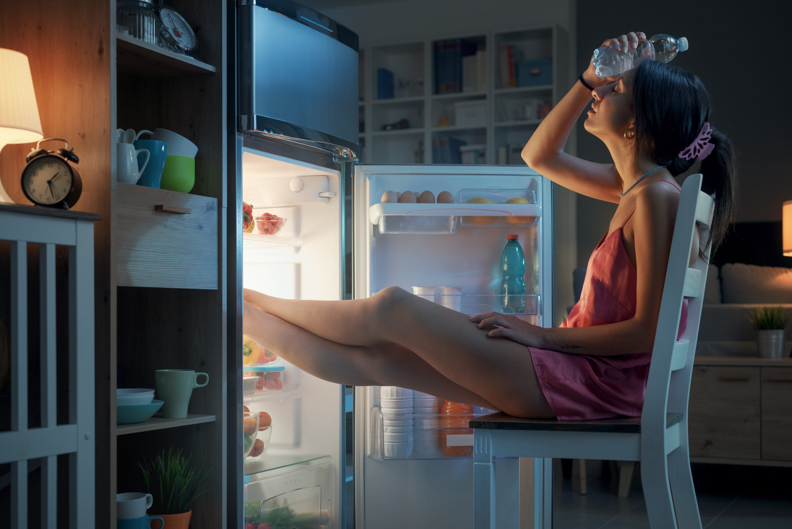 Femme souffrant de la chaleur en été, elle se repose les pieds dans le réfrigérateur et tient une bouteille d'eau