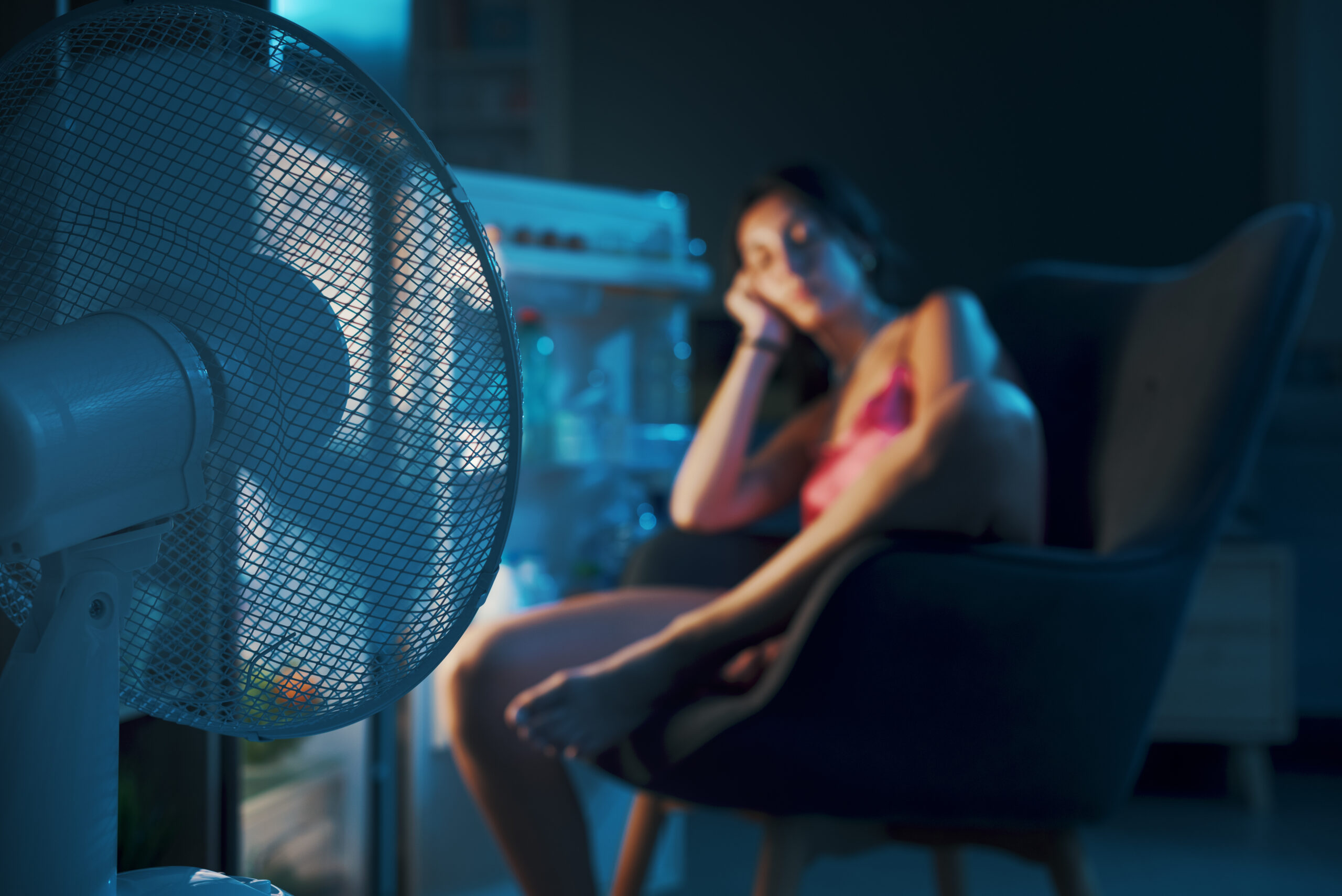 Femme épuisée souffrant de la chaleur pendant la canicule estivale, elle est assise devant le réfrigérateur ouvert et se rafraîchit
