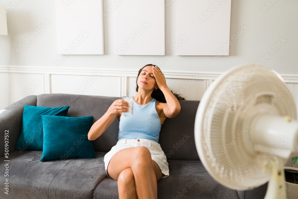 Femme épuisée souffrant de la chaleur pendant la canicule estivale, elle est assise devant le ventilateur ouvert et se rafraîchit